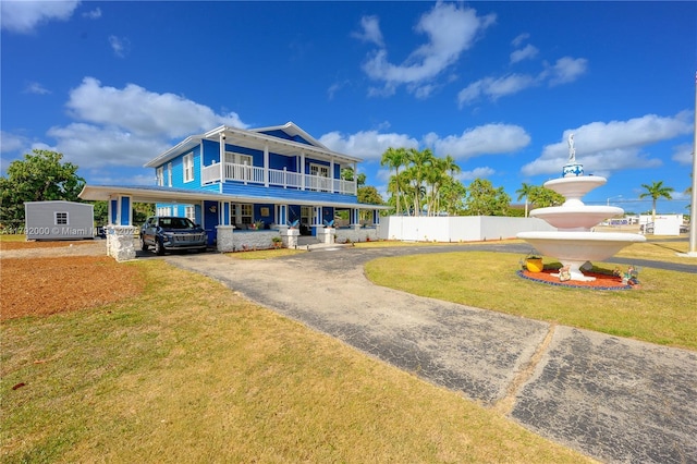 rear view of property with covered porch, fence, driveway, a balcony, and a lawn