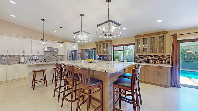 kitchen featuring stainless steel refrigerator with ice dispenser, a large island, backsplash, and under cabinet range hood