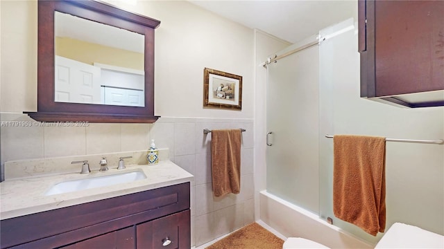bathroom with toilet, tile walls, bath / shower combo with glass door, and vanity