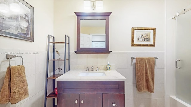 full bathroom featuring vanity, a shower, a wainscoted wall, and tile walls
