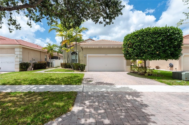 mediterranean / spanish house with a front yard, a garage, decorative driveway, a tiled roof, and stucco siding