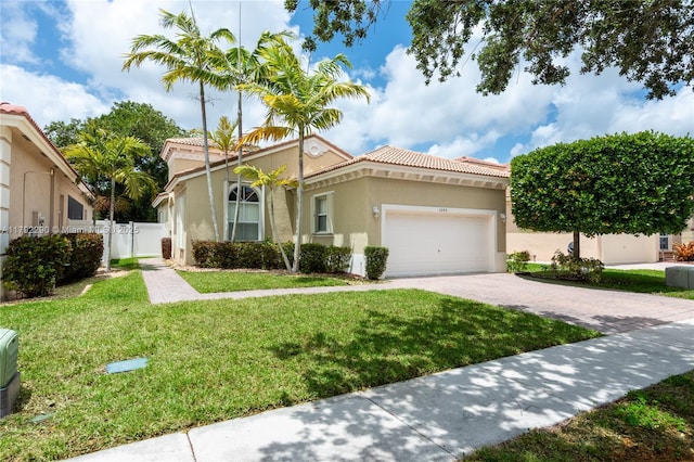 mediterranean / spanish home with a tile roof, a front yard, a garage, driveway, and stucco siding