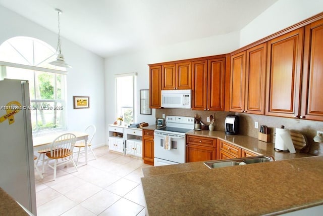 kitchen featuring light tile patterned floors, vaulted ceiling, white appliances, brown cabinetry, and hanging light fixtures