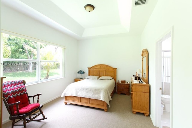bedroom with connected bathroom, light colored carpet, visible vents, a tray ceiling, and baseboards