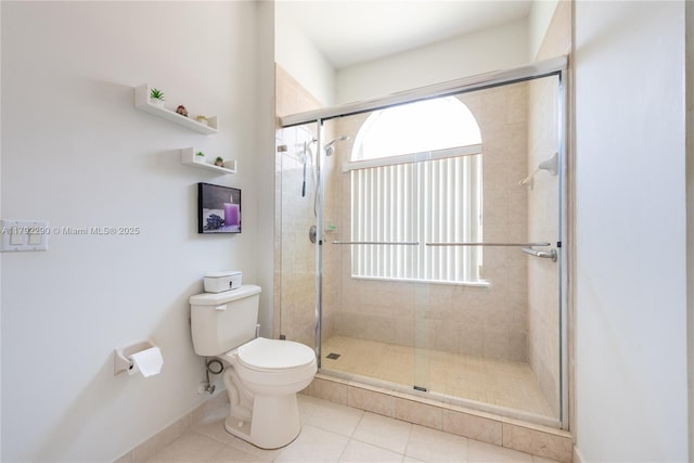 bathroom with tile patterned floors, toilet, a shower stall, and baseboards