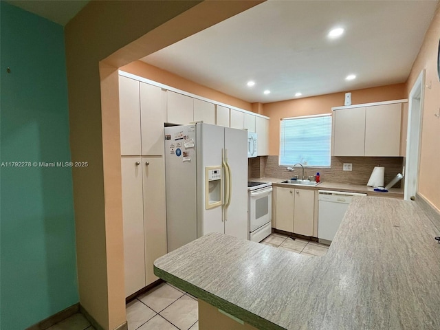 kitchen with a sink, light tile patterned flooring, tasteful backsplash, a peninsula, and white appliances