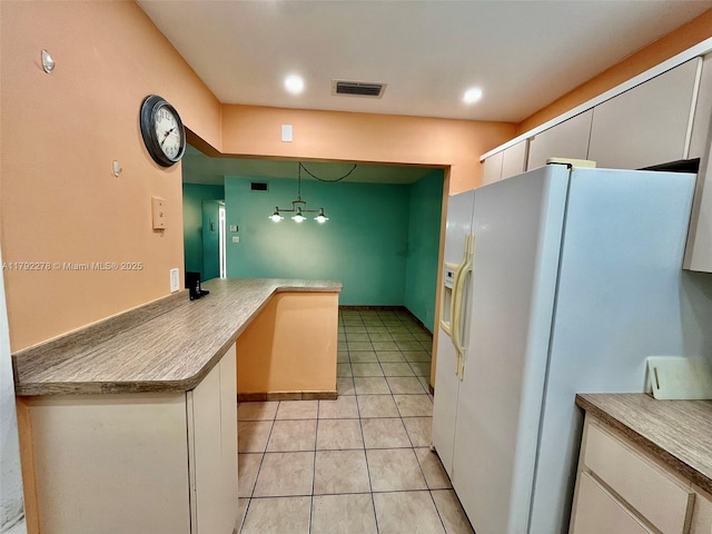 kitchen with light tile patterned floors, white refrigerator with ice dispenser, visible vents, a peninsula, and white cabinetry