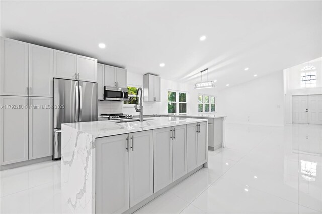 11069 Rios Rd, Boca Raton, FL 33498 - kitchen with light tile patterned flooring, light stone countertops, hanging light fixtures, stainless steel appliances, and a center island with sink