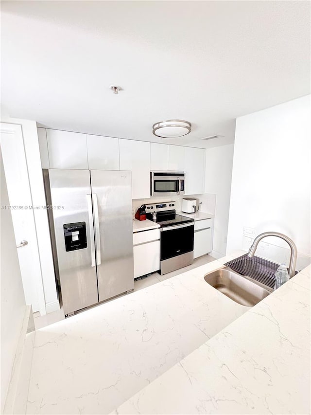kitchen featuring light stone countertops, a sink, stainless steel appliances, marble finish floor, and white cabinets