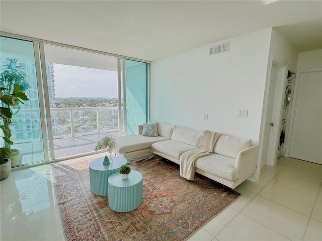 tiled living room featuring stacked washer and dryer, visible vents, and floor to ceiling windows