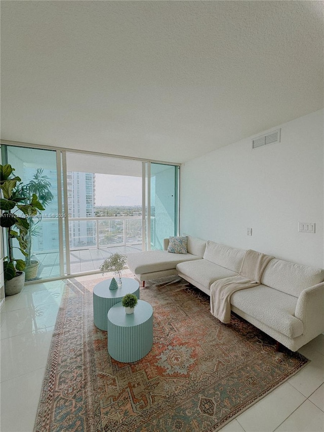 tiled living room with visible vents, a textured ceiling, and floor to ceiling windows