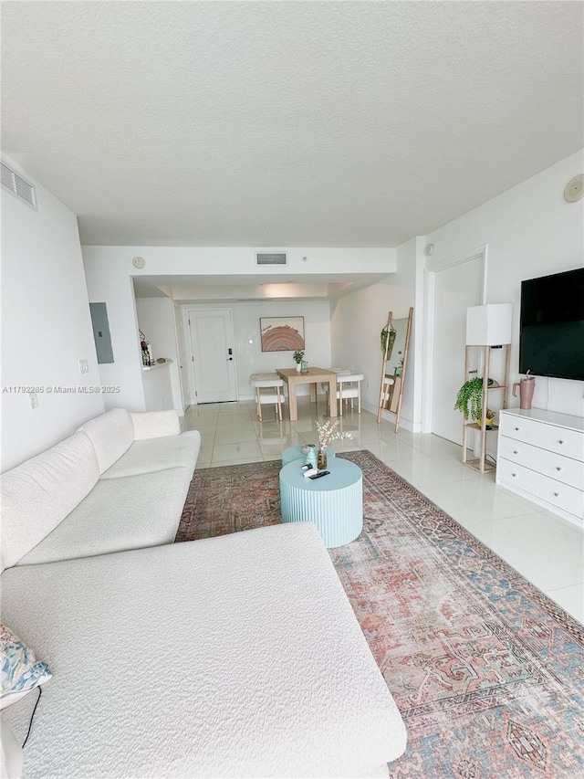tiled living area featuring visible vents, a textured ceiling, and electric panel