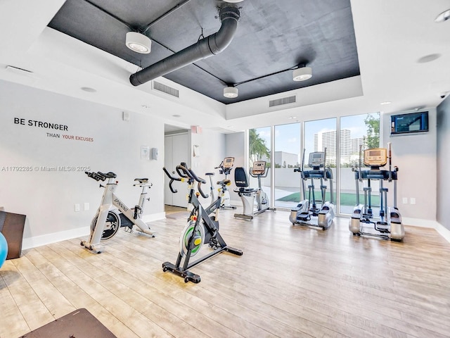 workout area featuring expansive windows, a raised ceiling, visible vents, baseboards, and wood finished floors