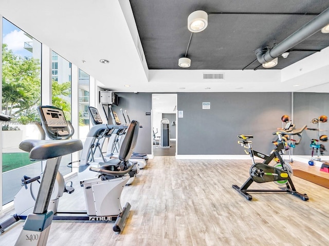 exercise room with wood finished floors, visible vents, a tray ceiling, and baseboards