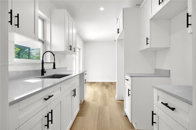 kitchen featuring recessed lighting, light wood-style flooring, light stone counters, a sink, and white cabinetry