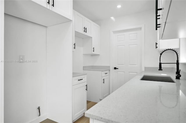 kitchen featuring light stone counters, white cabinets, a sink, recessed lighting, and light wood finished floors