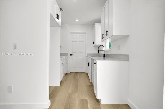 kitchen with light countertops, a sink, white cabinetry, and light wood-style floors