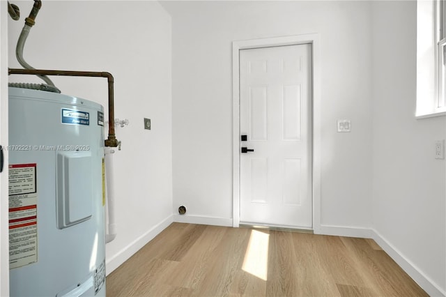 laundry room featuring light wood finished floors, water heater, laundry area, and baseboards