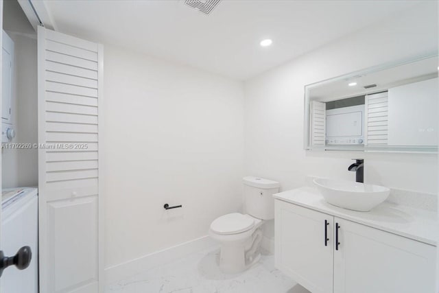bathroom featuring visible vents, stacked washing maching and dryer, toilet, vanity, and marble finish floor