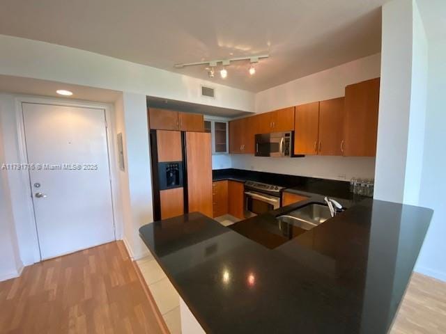 kitchen with a sink, brown cabinets, visible vents, dark countertops, and appliances with stainless steel finishes
