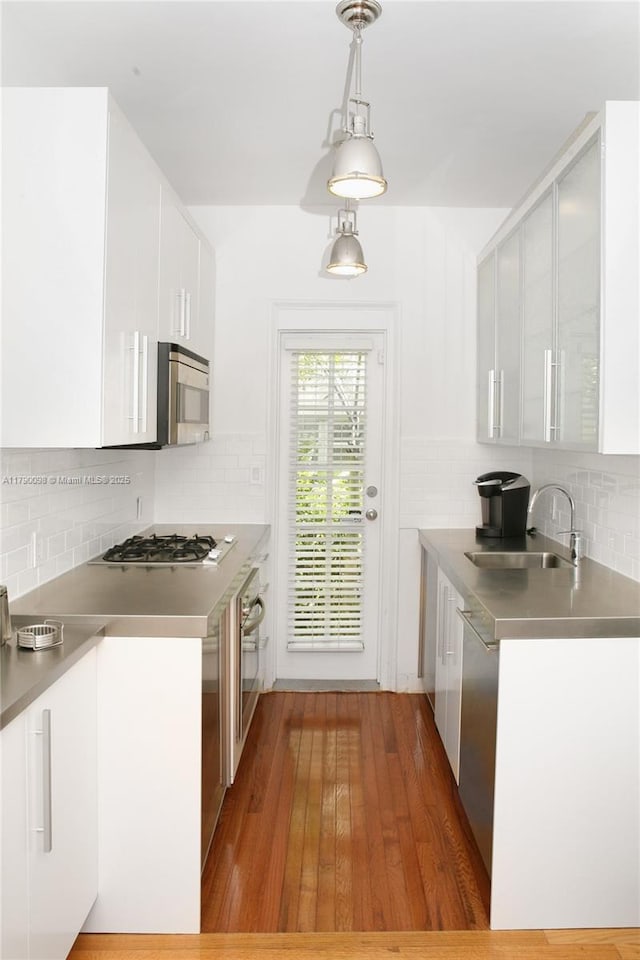 kitchen featuring white cabinets, a sink, appliances with stainless steel finishes, stainless steel countertops, and backsplash