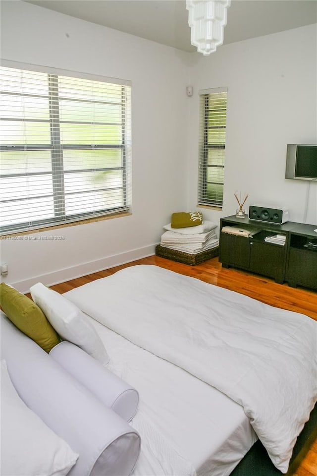 bedroom with an inviting chandelier, wood finished floors, and baseboards