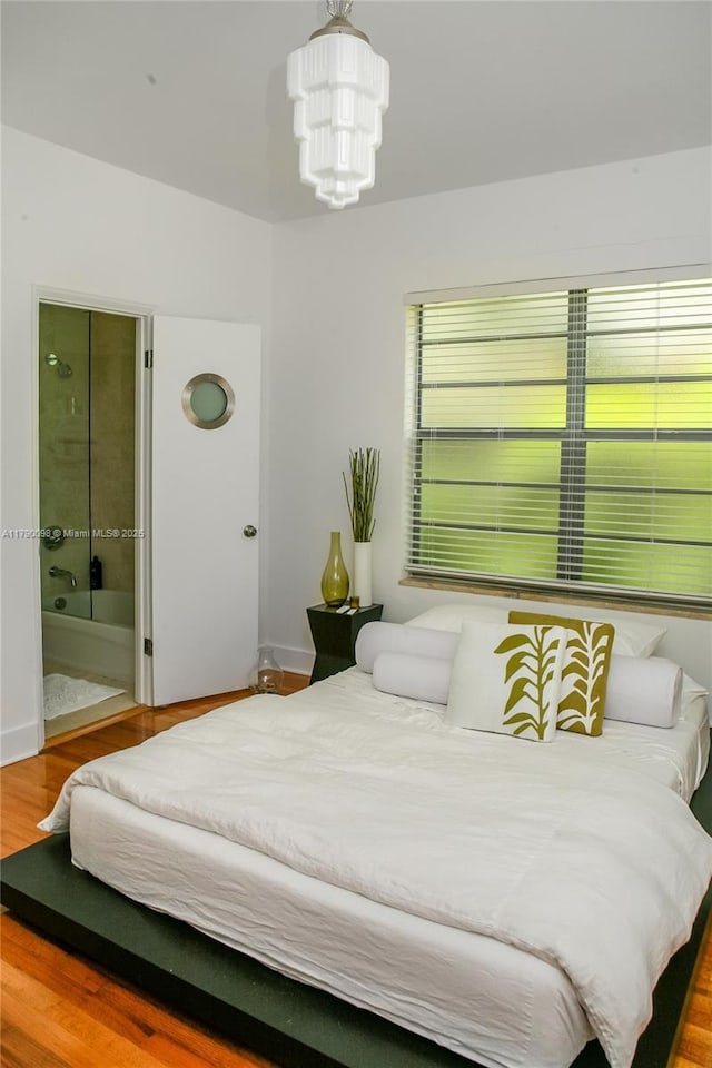 bedroom with wood finished floors, connected bathroom, a notable chandelier, and baseboards