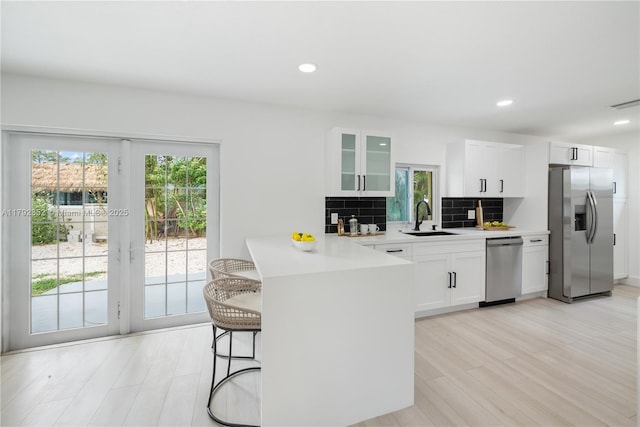 kitchen with glass insert cabinets, decorative backsplash, appliances with stainless steel finishes, a sink, and a peninsula