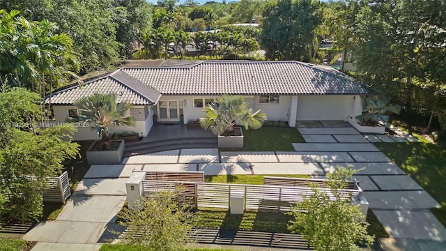 rear view of house with driveway, a tile roof, stucco siding, an attached garage, and fence