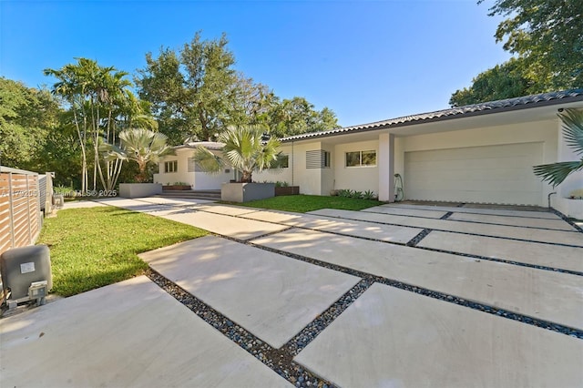 view of front of property with concrete driveway, a tiled roof, a front yard, an attached garage, and stucco siding