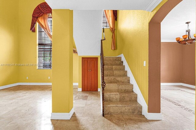 staircase with a healthy amount of sunlight, a notable chandelier, arched walkways, and baseboards