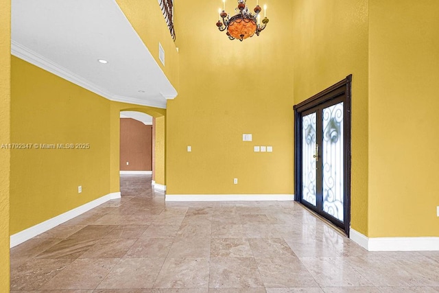 foyer featuring a high ceiling, an inviting chandelier, baseboards, ornamental molding, and arched walkways