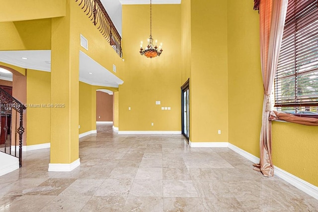 unfurnished living room featuring crown molding, a chandelier, baseboards, arched walkways, and a high ceiling
