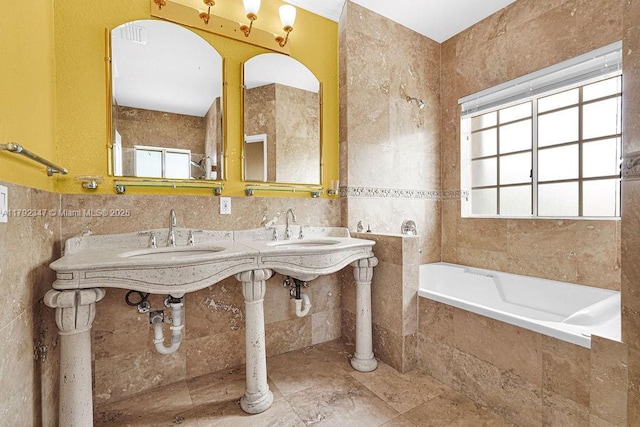 bathroom featuring tile walls, a wealth of natural light, tiled tub, and a sink
