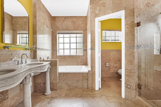 full bathroom with a sink, tiled bath, a stall shower, toilet, and tile walls