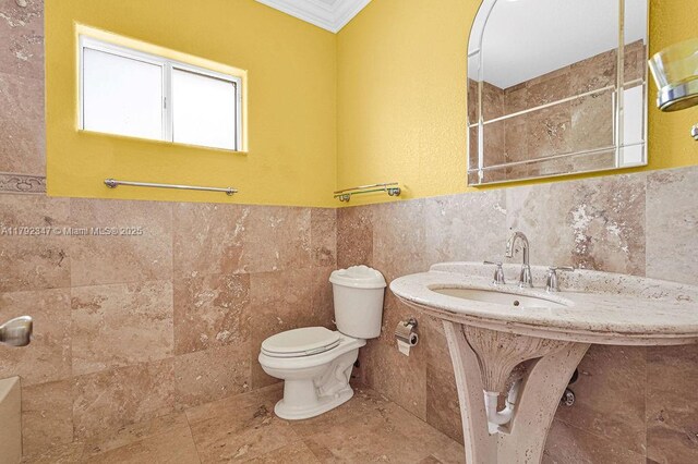 bathroom with crown molding, tile walls, toilet, a sink, and a shower