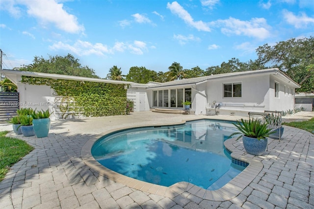 rear view of property with stucco siding, an outdoor pool, and a patio area