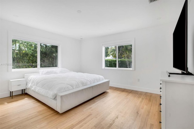 bedroom featuring multiple windows, baseboards, and light wood-style floors