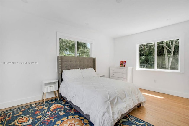 bedroom with wood finished floors, baseboards, and multiple windows