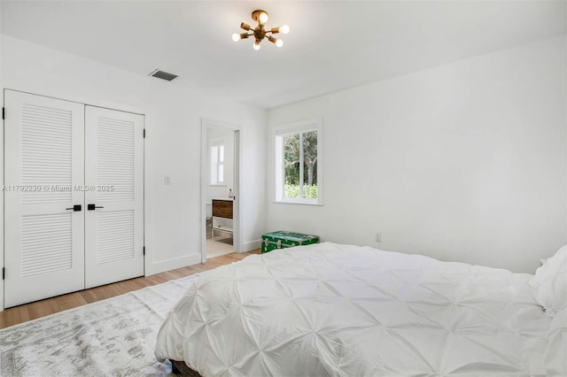 bedroom with visible vents, ensuite bathroom, baseboards, wood finished floors, and a notable chandelier
