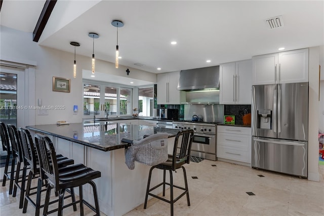 kitchen with wall chimney range hood, a breakfast bar area, tasteful backsplash, visible vents, and stainless steel appliances