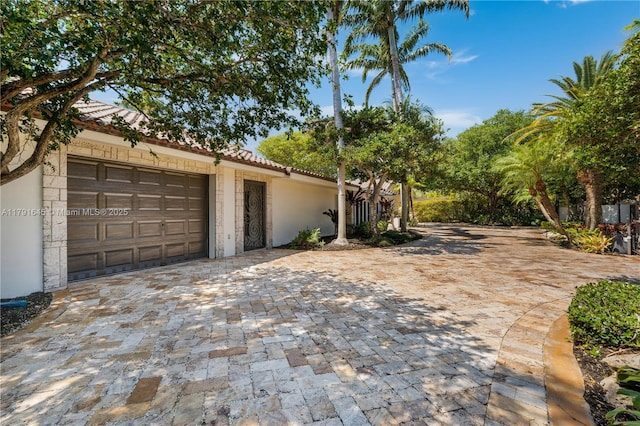 view of side of property with a garage, a tile roof, stucco siding, and decorative driveway