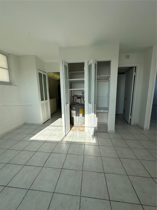 unfurnished bedroom featuring baseboards, electric water heater, light tile patterned flooring, and two closets