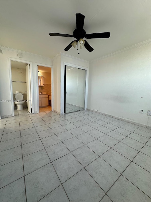unfurnished bedroom featuring light tile patterned floors, crown molding, ceiling fan, ensuite bathroom, and a closet