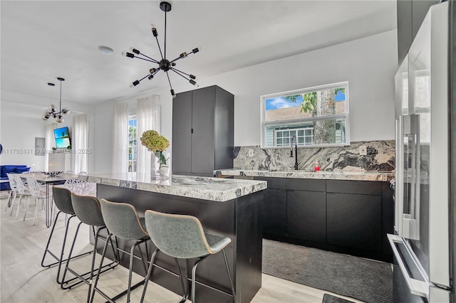 kitchen with a breakfast bar area, light wood-style flooring, an inviting chandelier, and high quality fridge