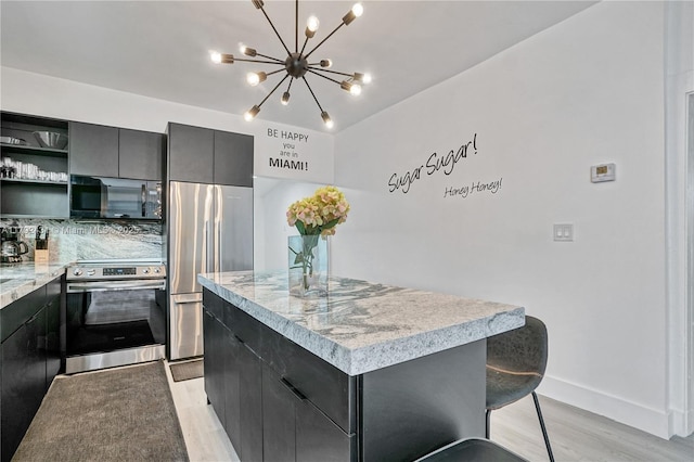 kitchen with light wood-style flooring, a notable chandelier, appliances with stainless steel finishes, a kitchen island, and dark cabinetry