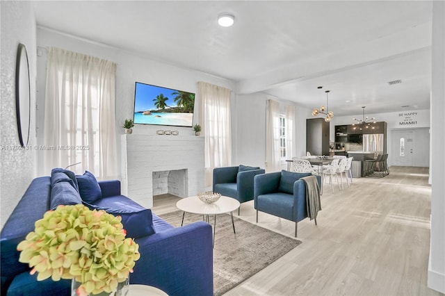 living area with beamed ceiling, a fireplace, a notable chandelier, visible vents, and light wood-style flooring