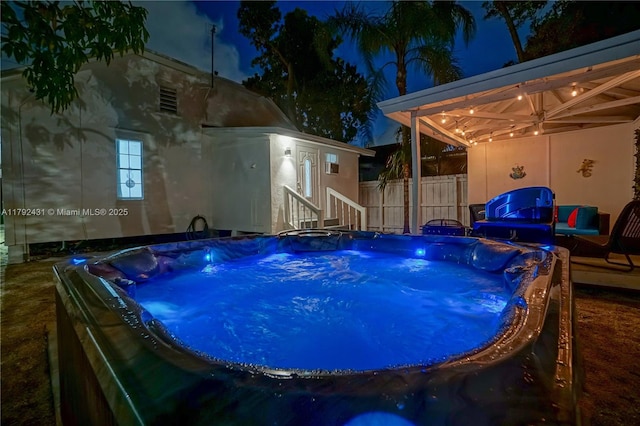 pool at night featuring fence and a hot tub