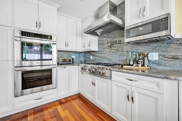 4701 Garfield St, Hollywood, FL 33021 - kitchen with white cabinetry, stainless steel appliances, wall chimney exhaust hood, stone counters, and backsplash