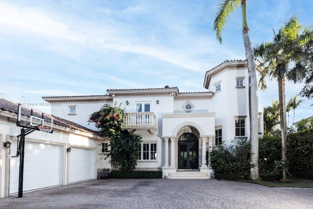 mediterranean / spanish-style home with a garage, french doors, a balcony, and stucco siding